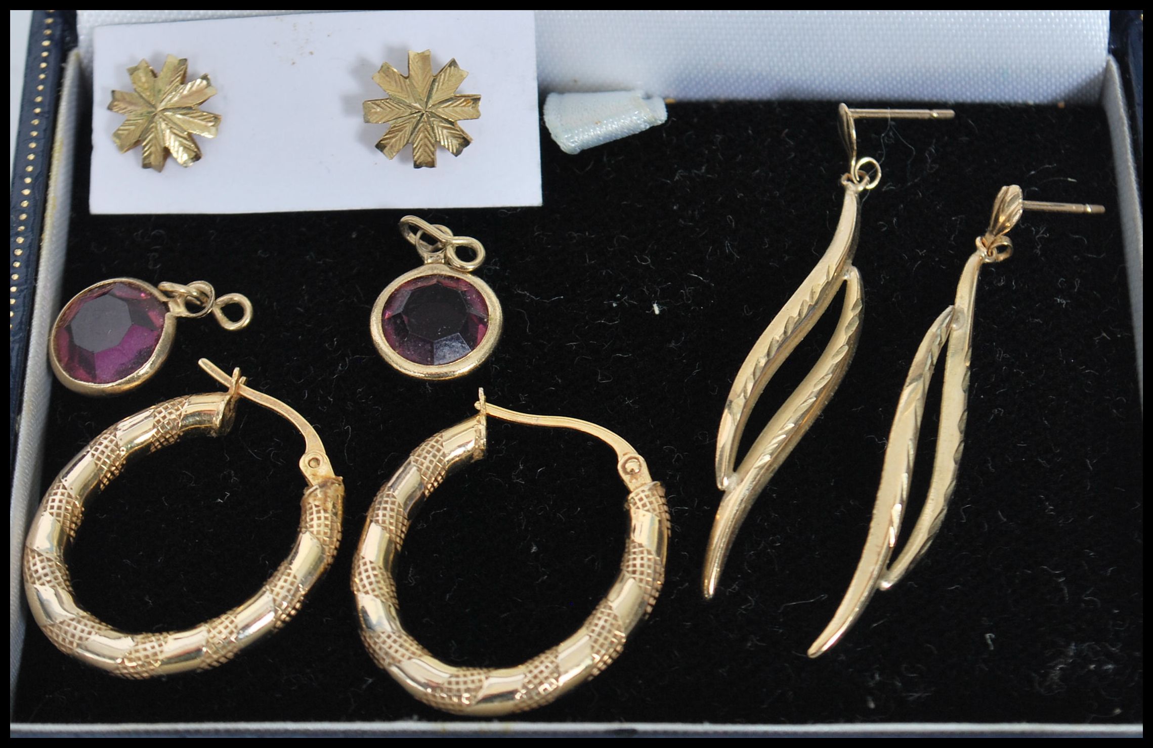 A group of 9ct gold earrings to include an engraved hoop pair, purple stone drop pair, star pair