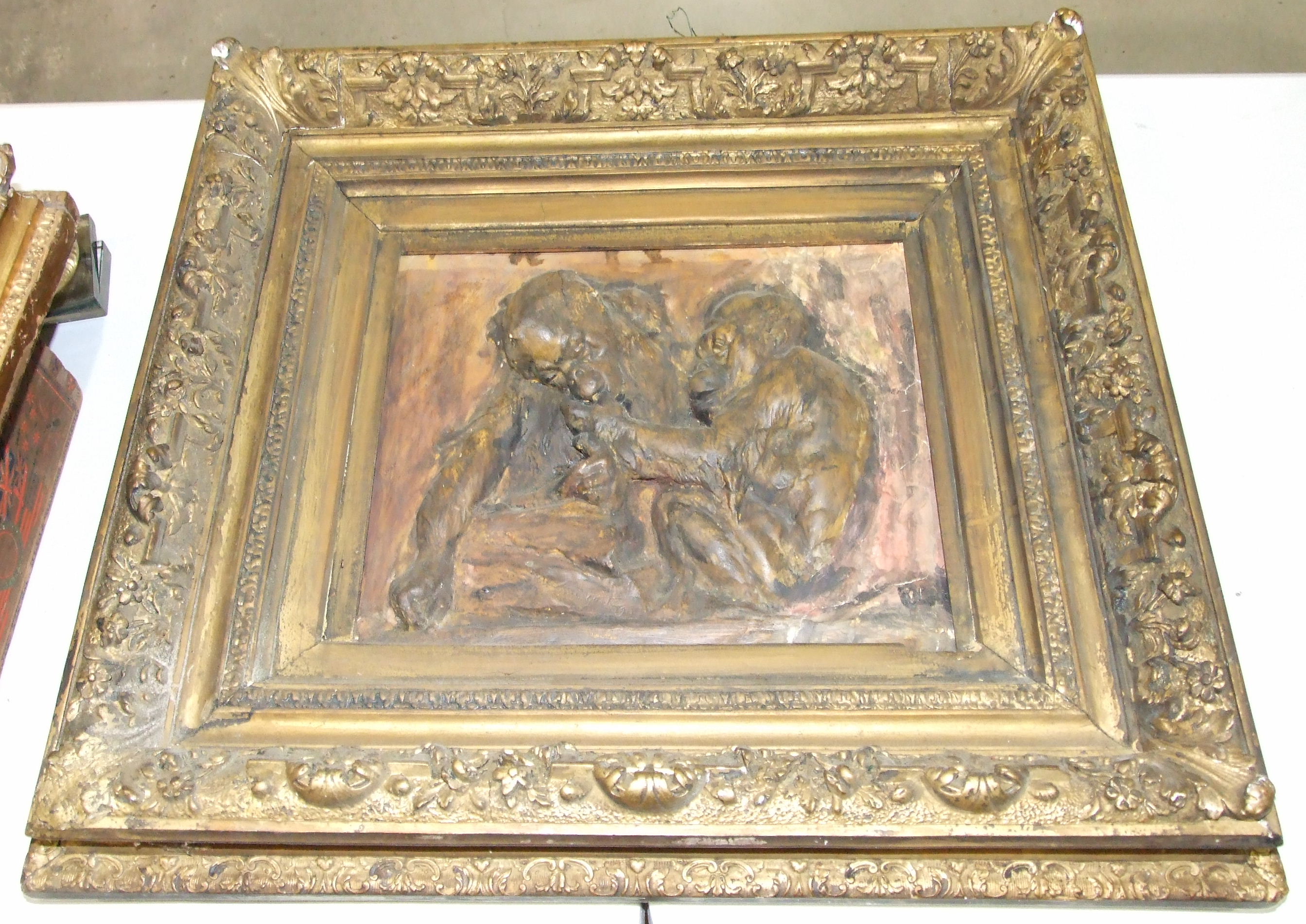 A carved plaster panel depicting two monkeys, in gilt frame, indistinctly-signed, 34 x 42cm, 64 x