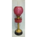 A Late-Victorian oil lamp, the cranberry glass reservoir on brass reeded column and stepped circular