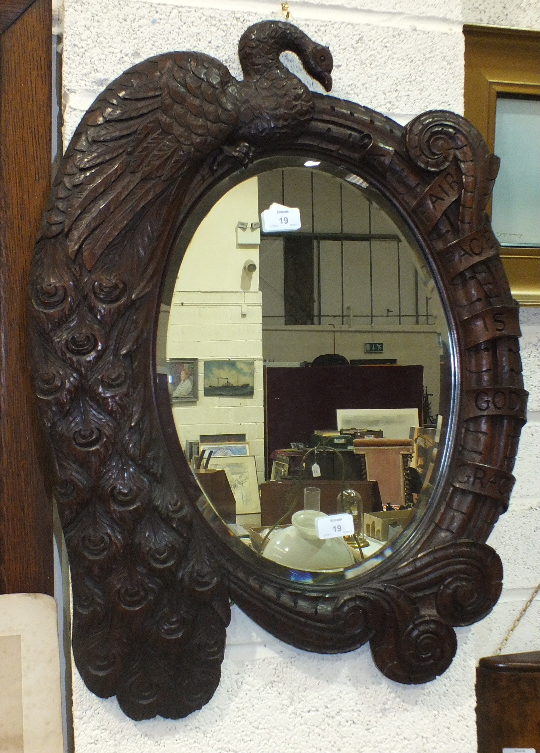 An oval bevelled mirror plate within a hardwood frame carved with a Peacock and engraved 'A Fair