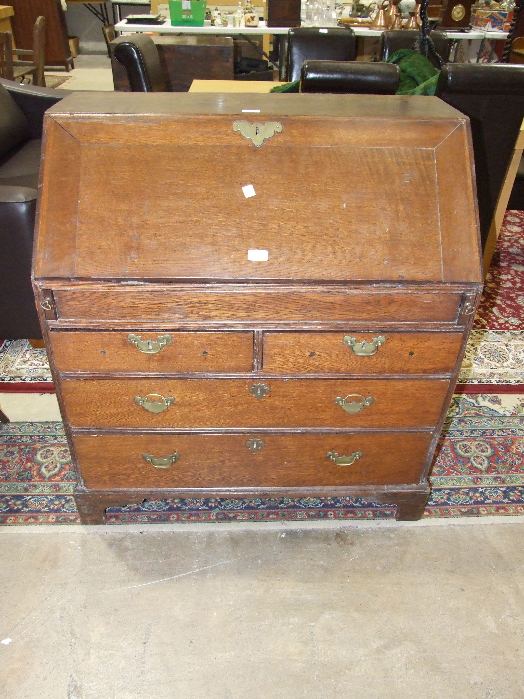 An antique oak bureau, the fall front with fitted interior above three graduated drawers on