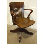 A 1920/30's oak revolving tilt action office armchair with slatted back and shaped seat, on