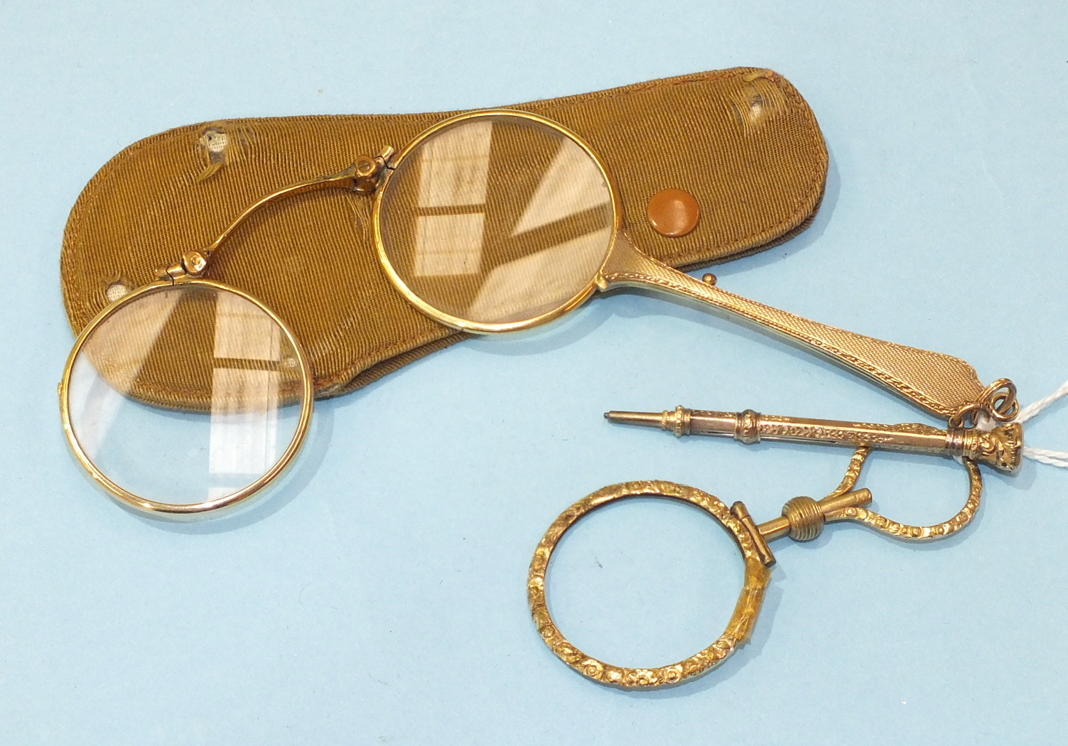 A pair of gold plated folded lorgnettes, cased, a gold plated eye glass (af), and a small gold