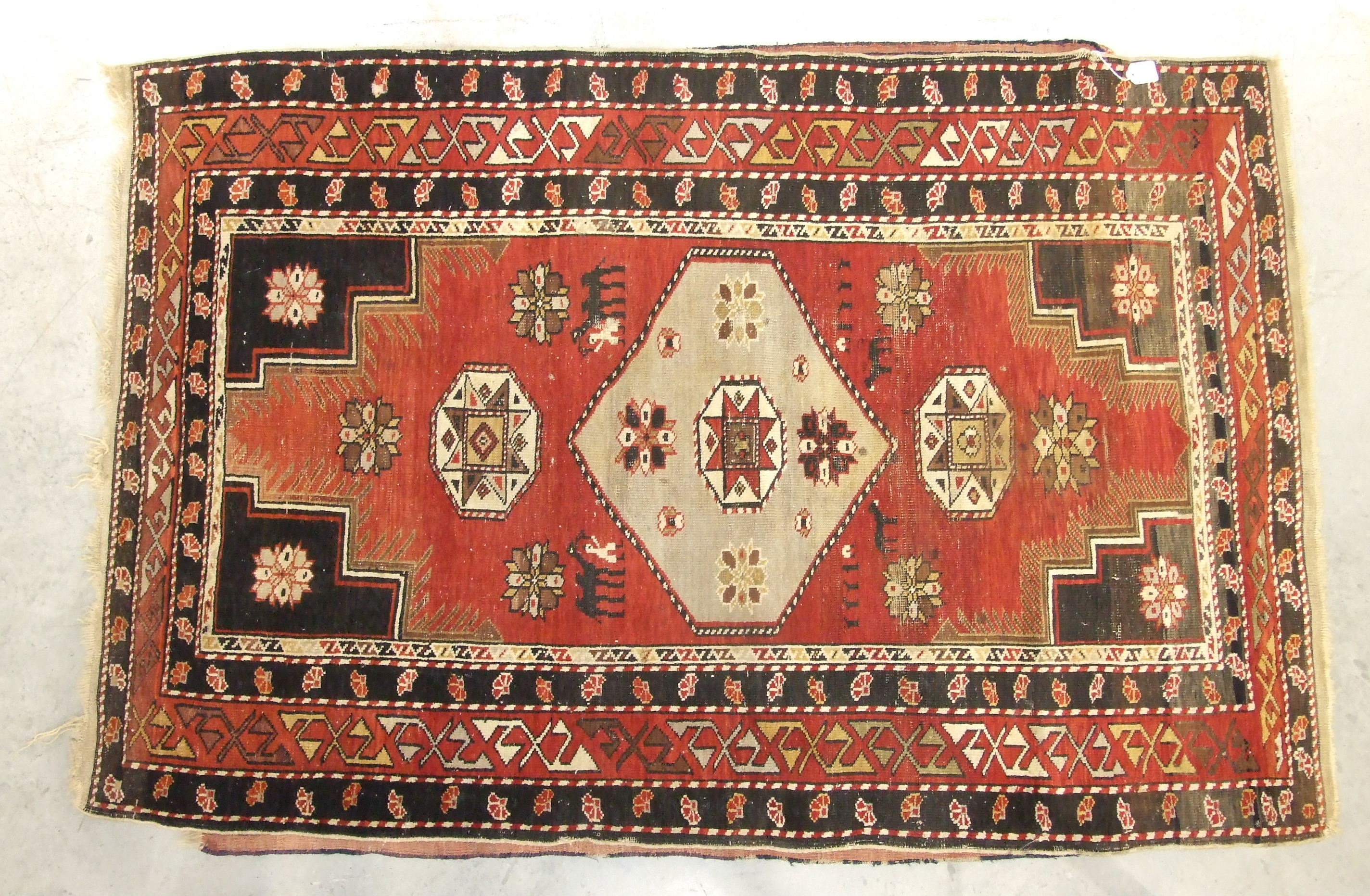 A mid-20th century wool rug, red field with central hexagonal medallions, figures leading camels and