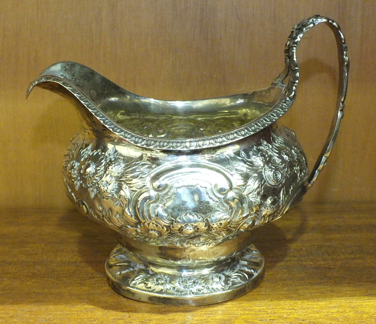 A George IV silver cream jug of lobed form, with leaf and floral embossed decoration, on circular