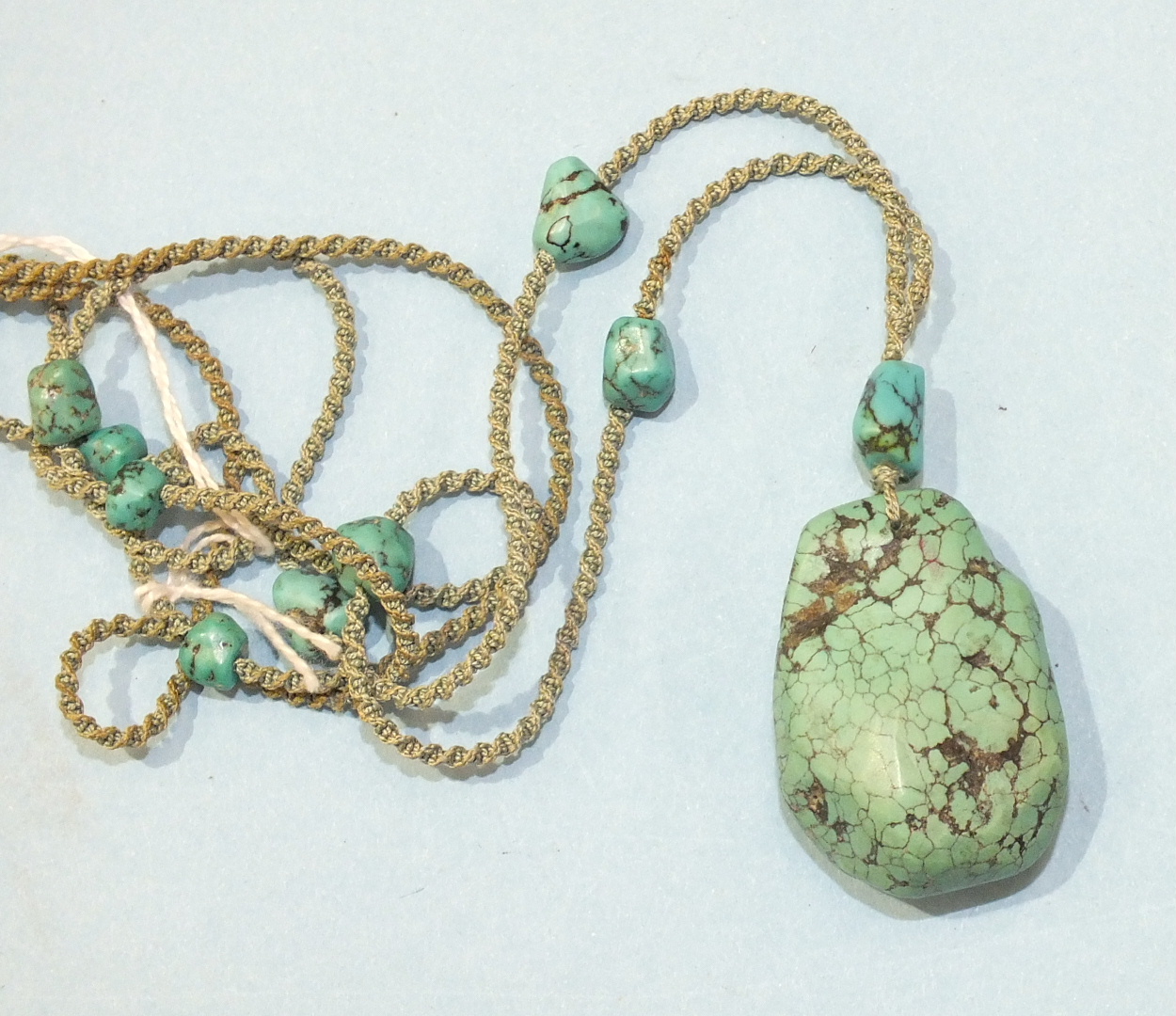 A Chinese turquoise matrix pendant suspended on a silk cord interspersed with turquoise matrix