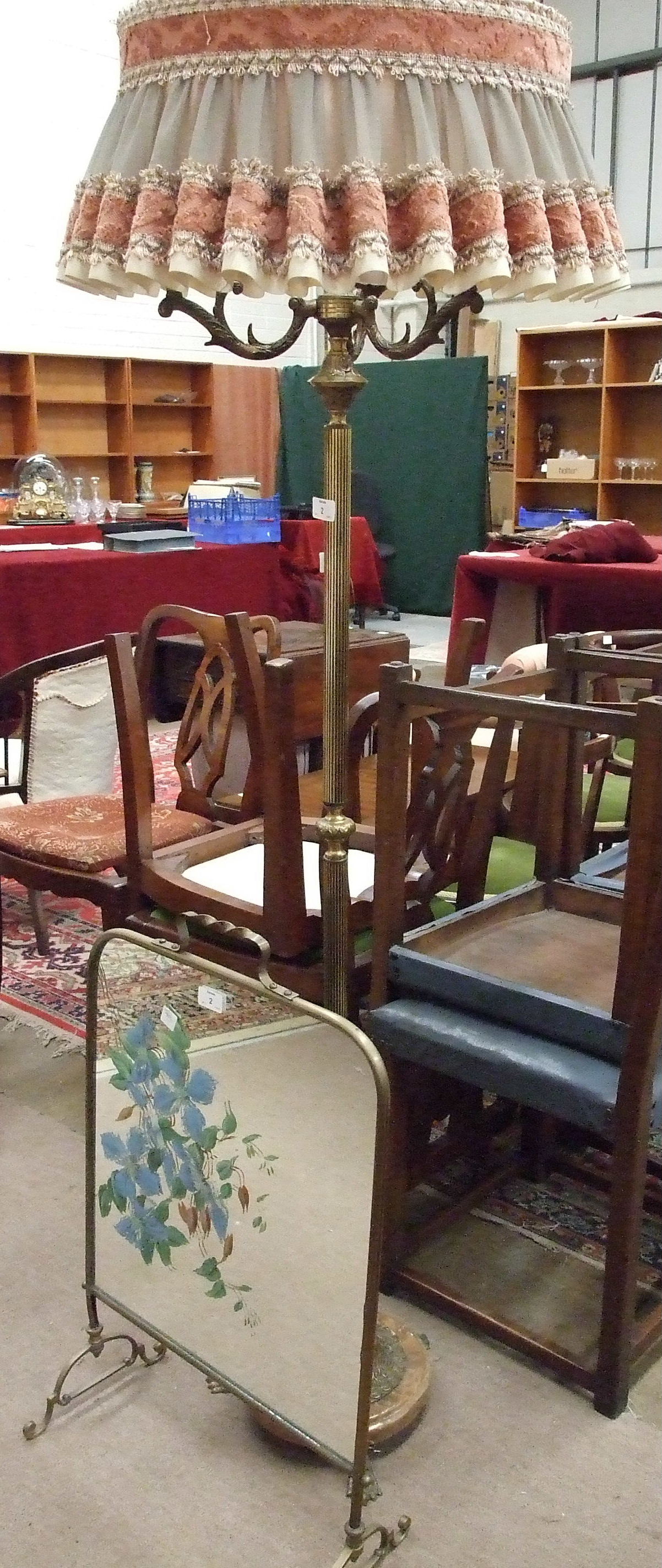 A brassed standard lamp on circular base with three claw feet, a brass framed mirrored fire screen