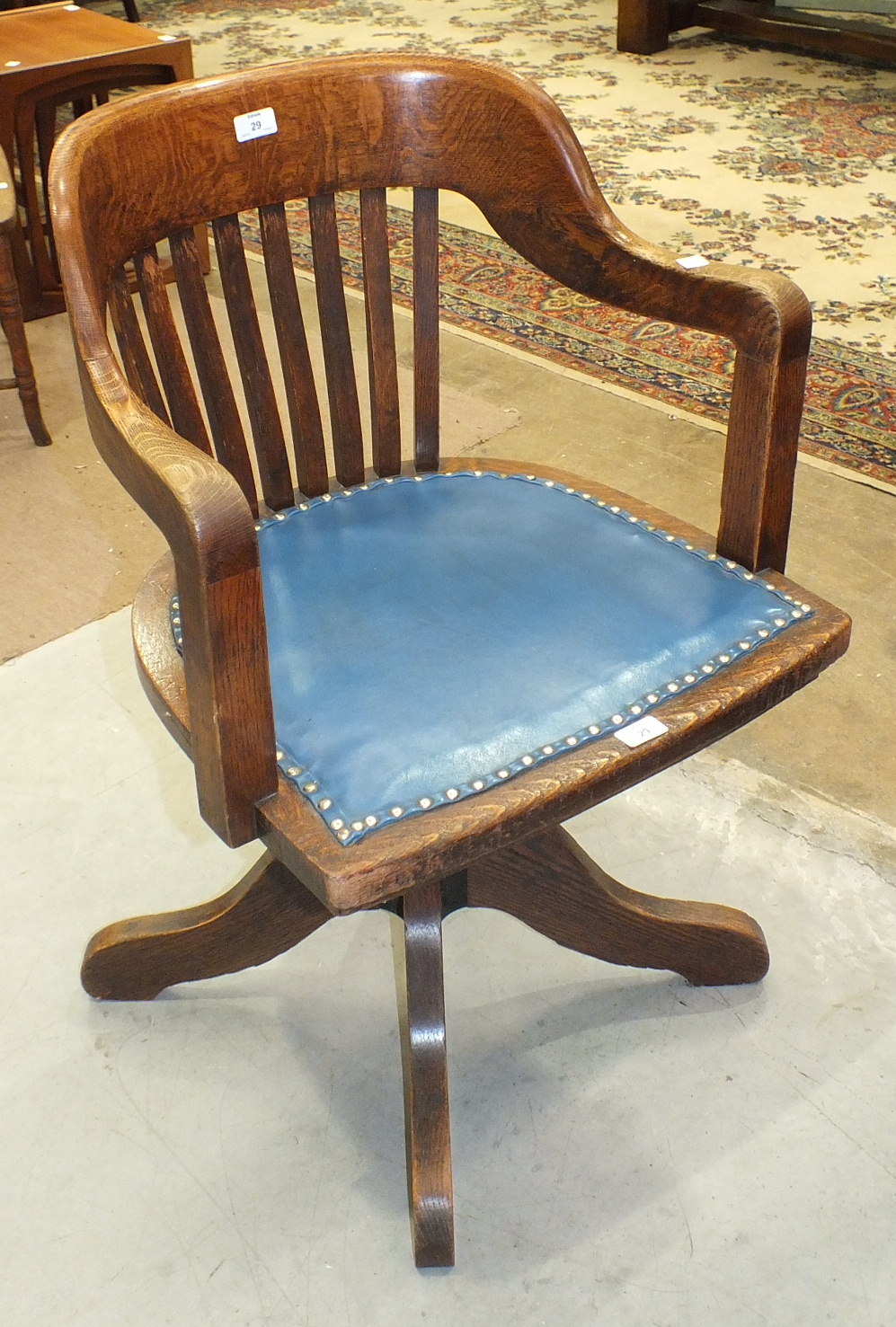 A 1920's/1930's oak revolving tilt-action office armchair with slatted back and shaped seat, on