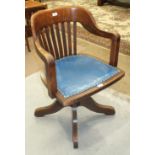 A 1920's/1930's oak revolving tilt-action office armchair with slatted back and shaped seat, on