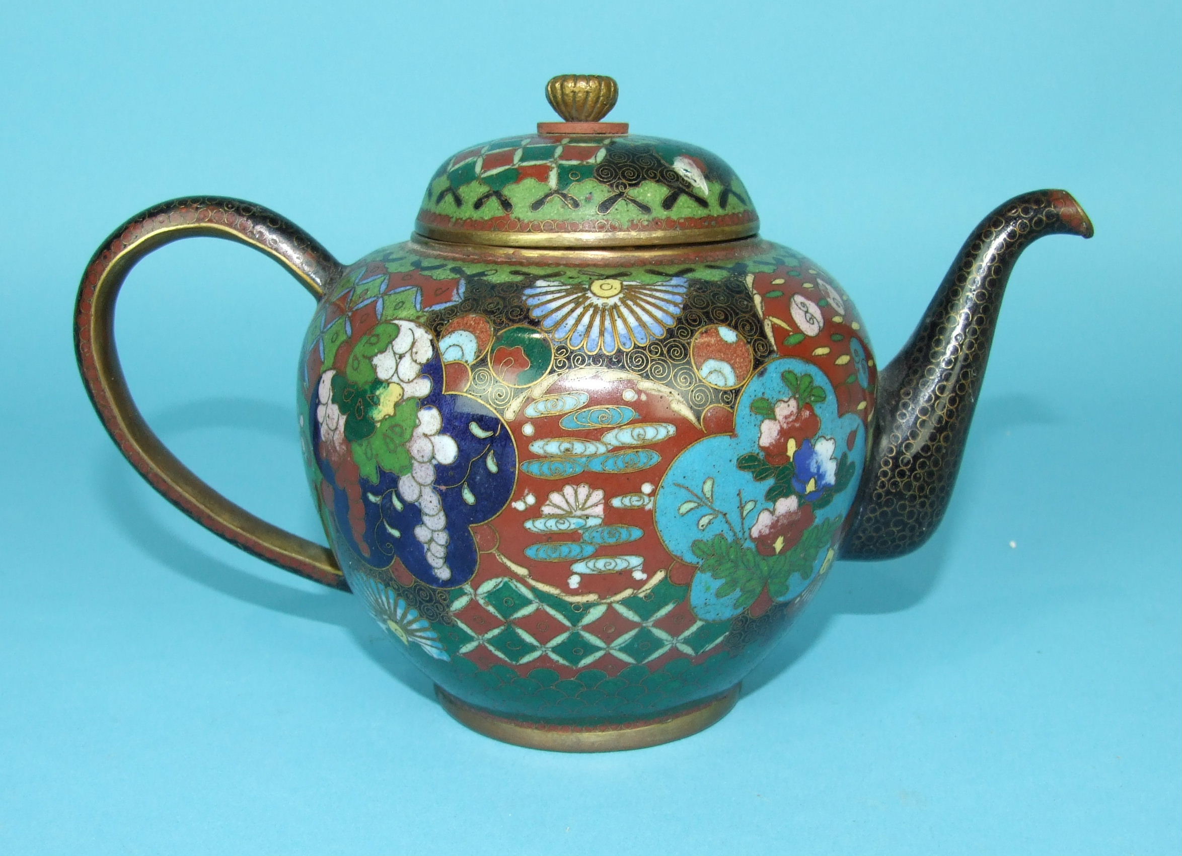 A 19th century Chinese cloisonné teapot and cover decorated with panels of flowers, on a brocade