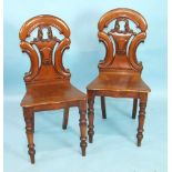 A pair of Victorian walnut hall chairs with pierced shaped backs and solid seats, on turned front