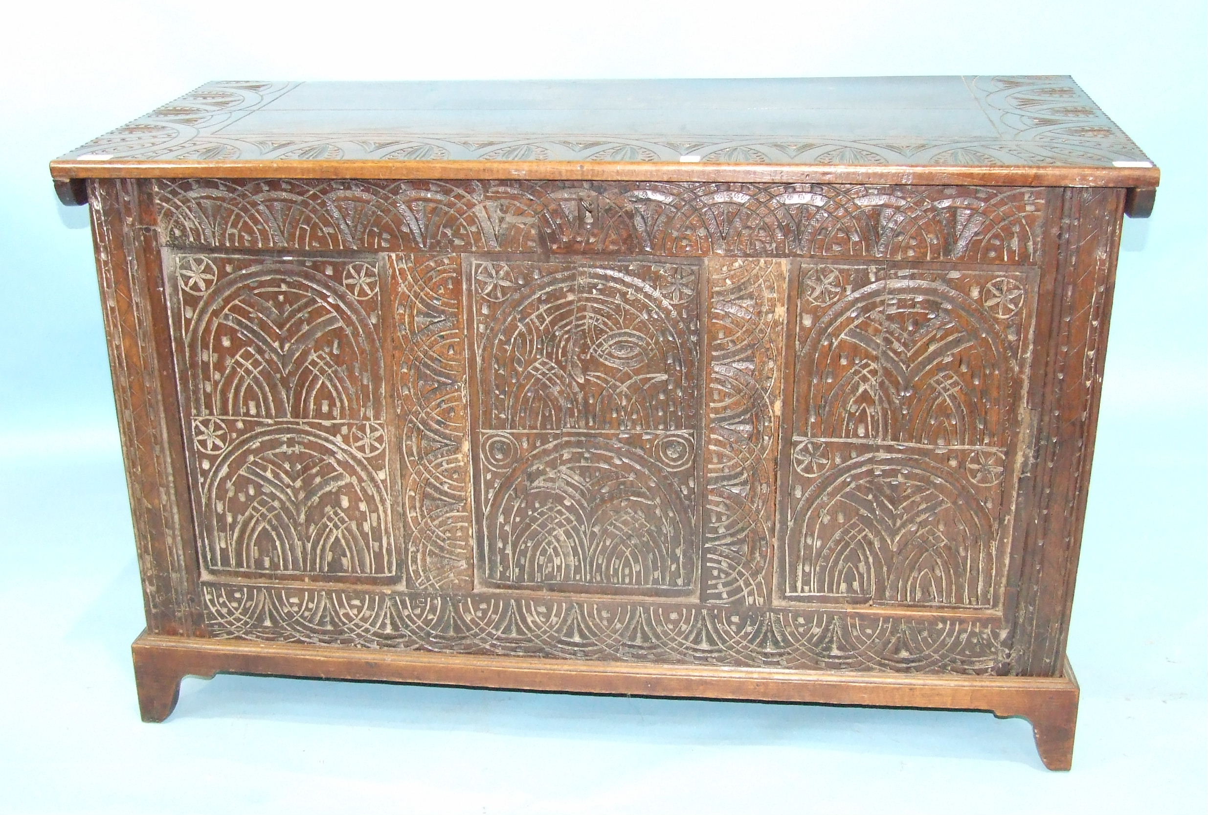 An antique oak coffer, the later top above carved front panels and later bracket feet, 127cm wide,