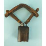 An antique metal goat bell suspended by leather straps from a wooden yoke, 27cm.