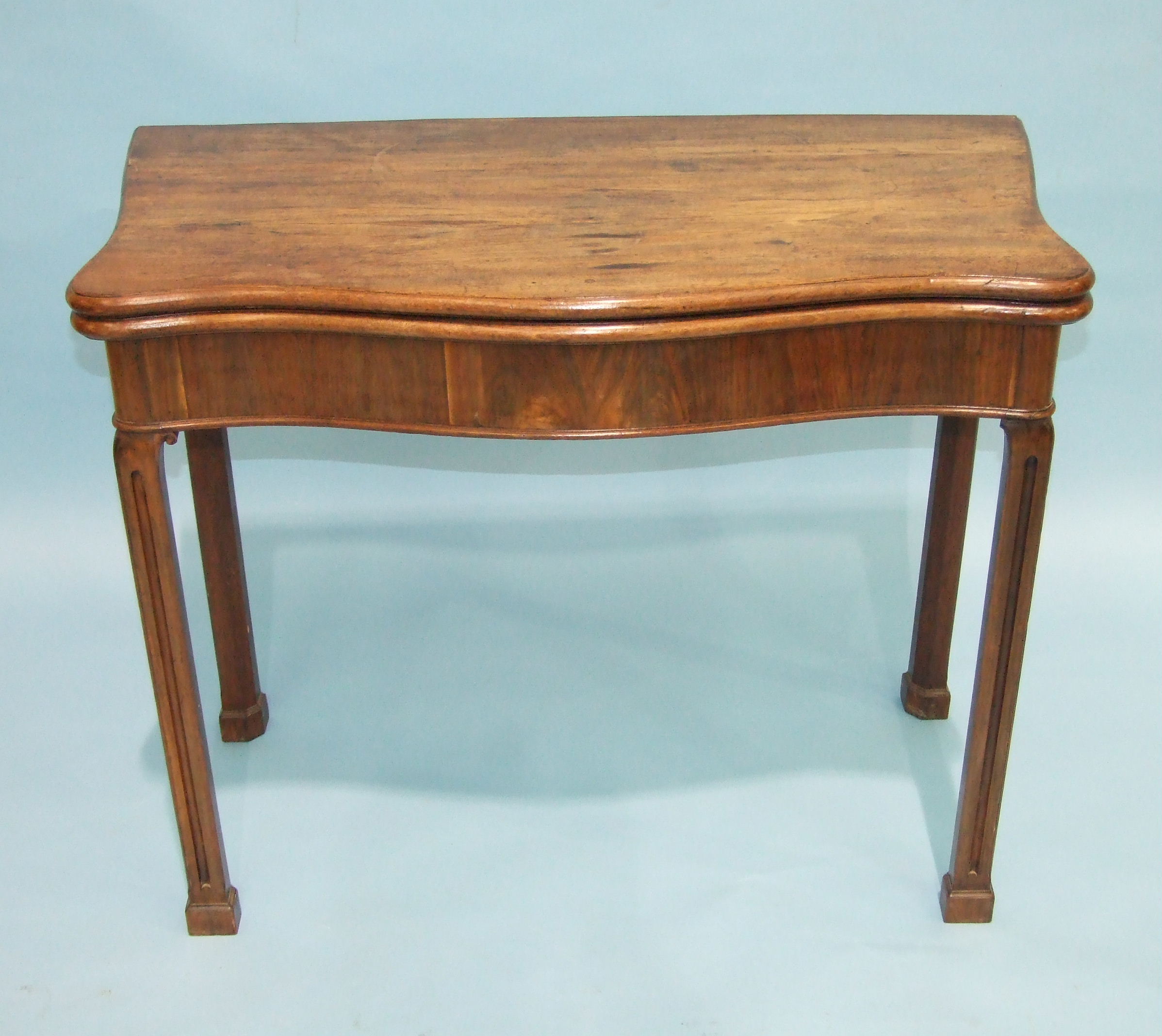 A Georgian mahogany serpentine fold-over card table, the top above a serpentine frieze, on fluted