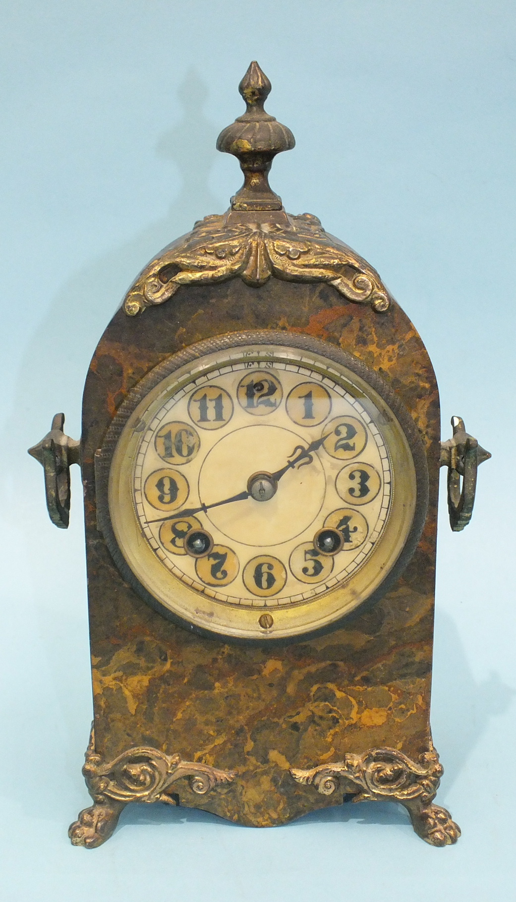 A simulated marble and gilt metal mantel clock of arch form with metal finial, carrying handle and