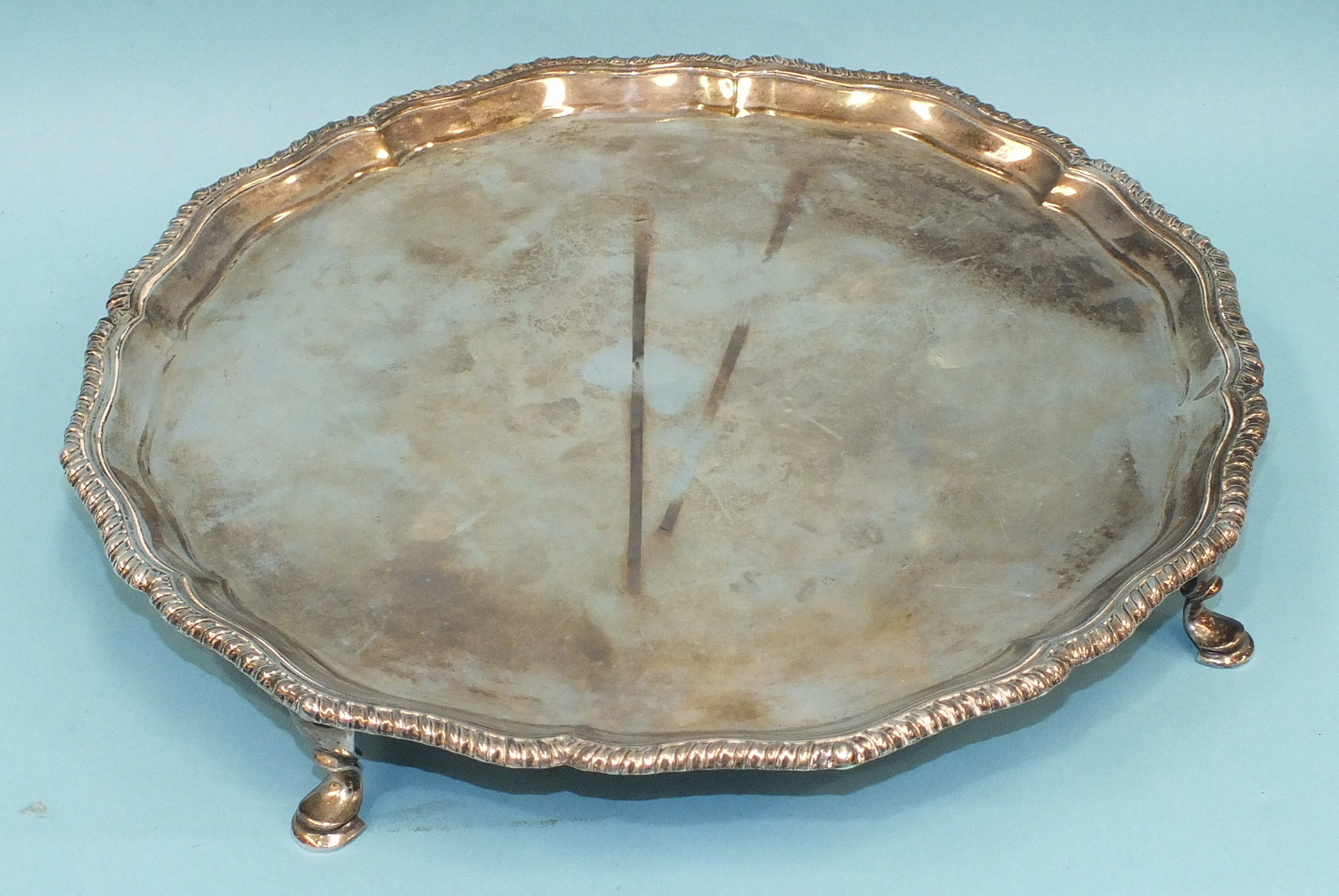 A circular salver with gadrooned border, on four tab feet, 27cm diameter, London 1926, ___20oz.