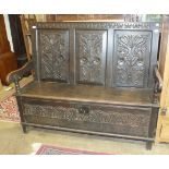 An oak settle, the carved panelled back and lift seat with arms, 145cm wide.