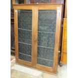 An Edwardian teak display notice board having a pair of glazed doors, 125cm high, 96cm wide.