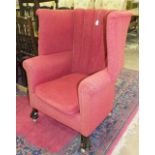 A large upholstered winged tub armchair on carved wood feet.