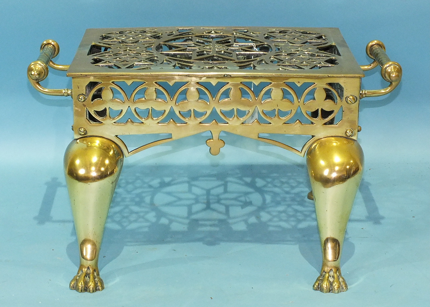 A brass two-handled footman with pierced top, on cabriole legs and paw feet, 54cm wide, 29cm high,