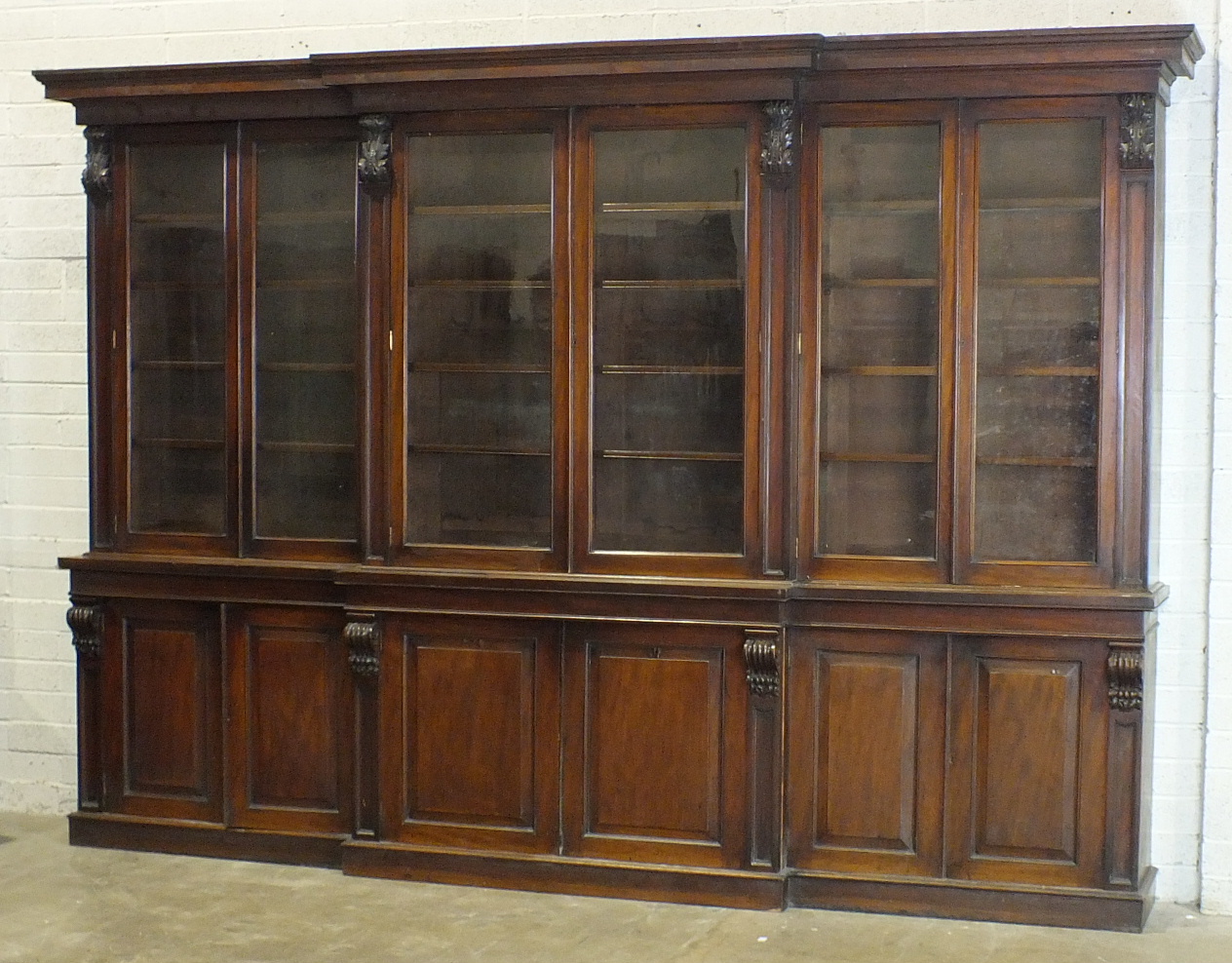 A large Victorian mahogany breakfront bookcase, the moulded stepped cornice supported by carved