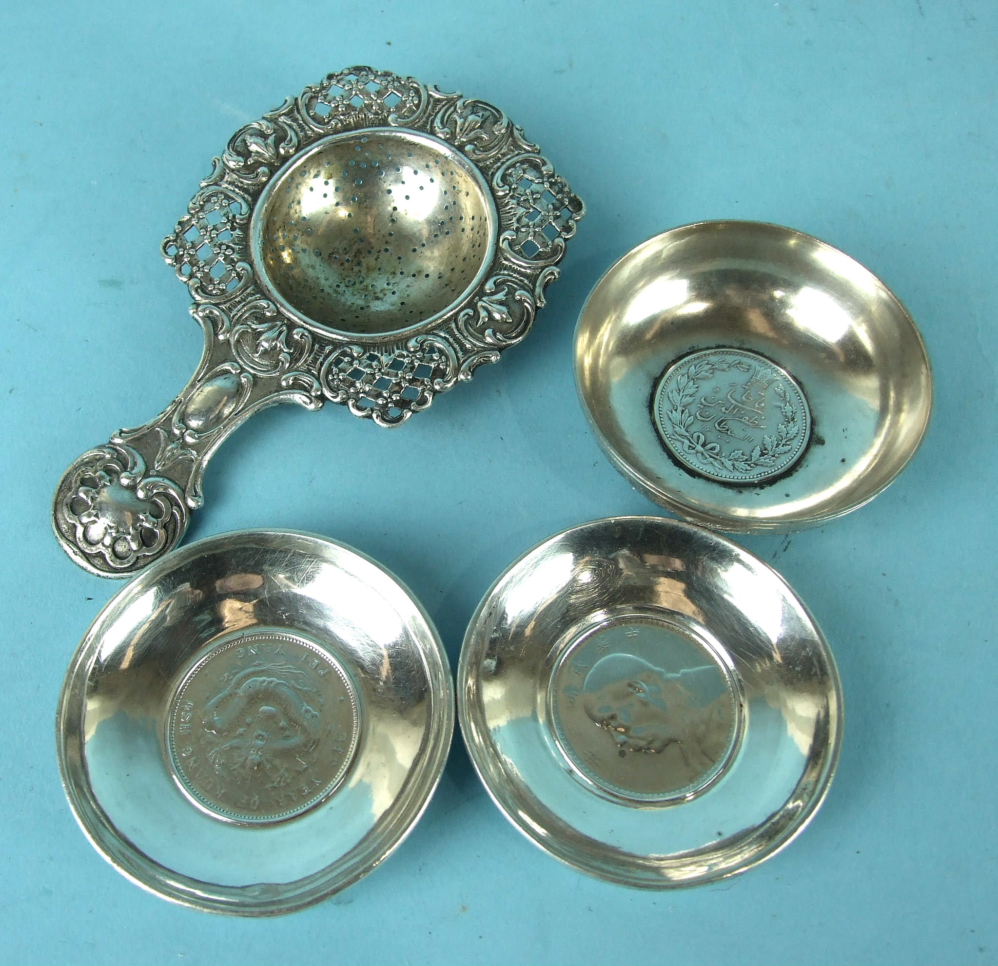 A Continental white metal tea strainer with pierced foliate border and handle, 14cm long and three