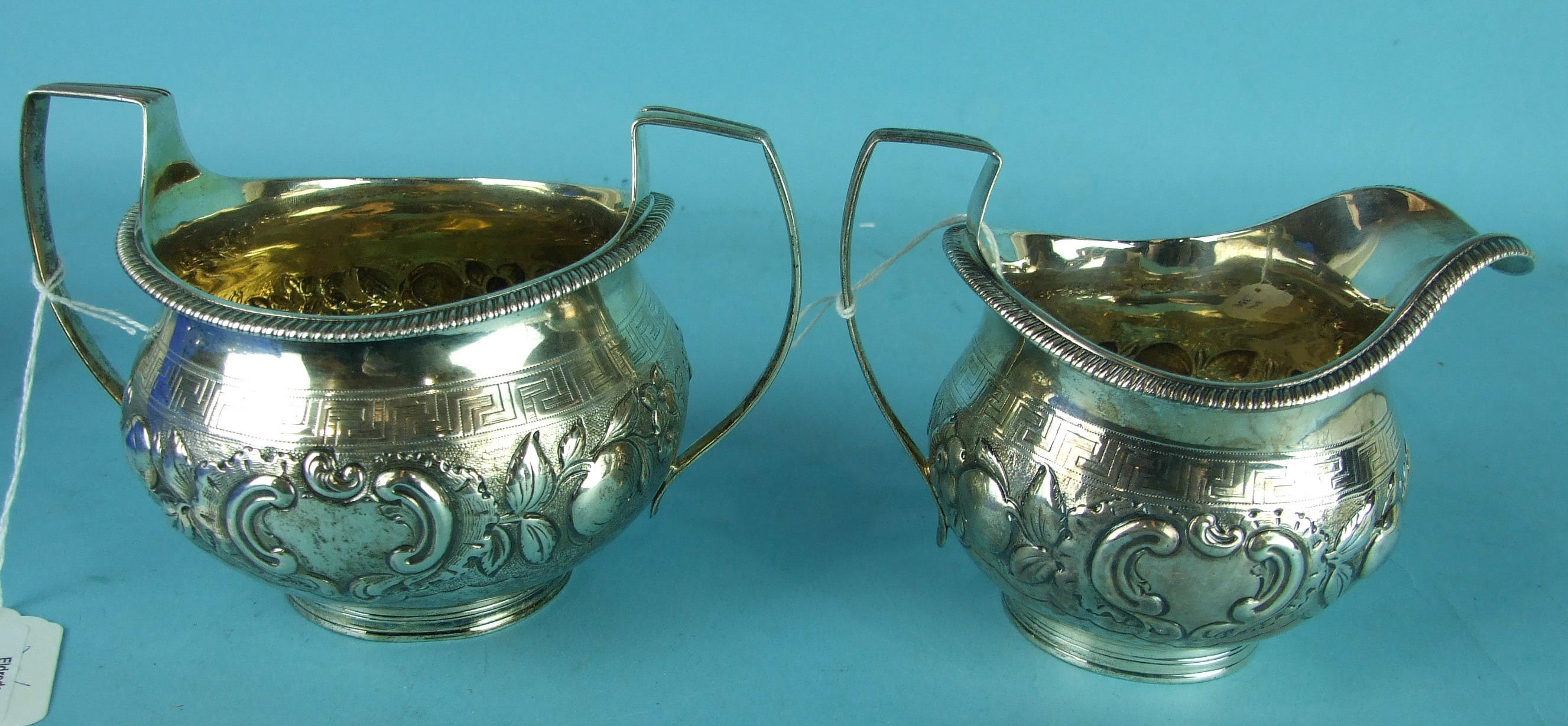 A George III sugar bowl and cream jug of circular bellied form, embossed with fruit and flowers