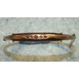 An Edwardian 9ct gold hinged bangle set three round cut rubies and two diamond points, 4.8g.