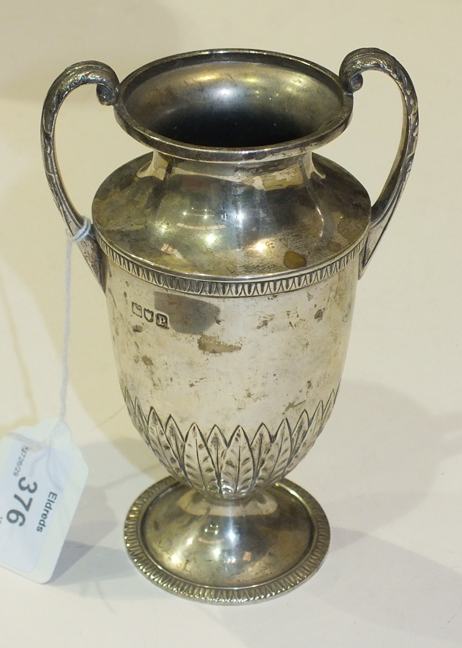 A silver urn with leaf capped scroll handles on loaded base, 16cm high, London 1910.
