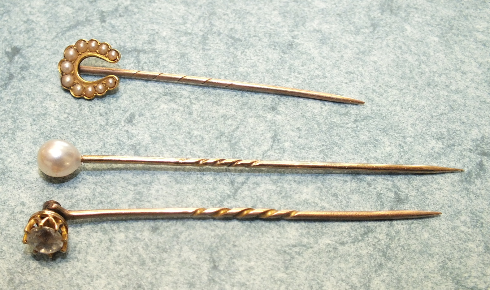 Three 19th century stick pins, one set a white paste stone, one a cultured pearl and one a pearl set