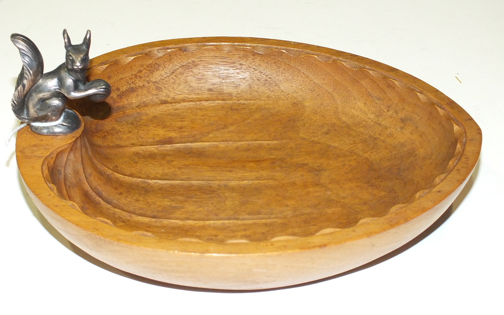 An ash wood nut bowl in the shape of a hazel nut surmounted by a silver squirrel, 20cm long.