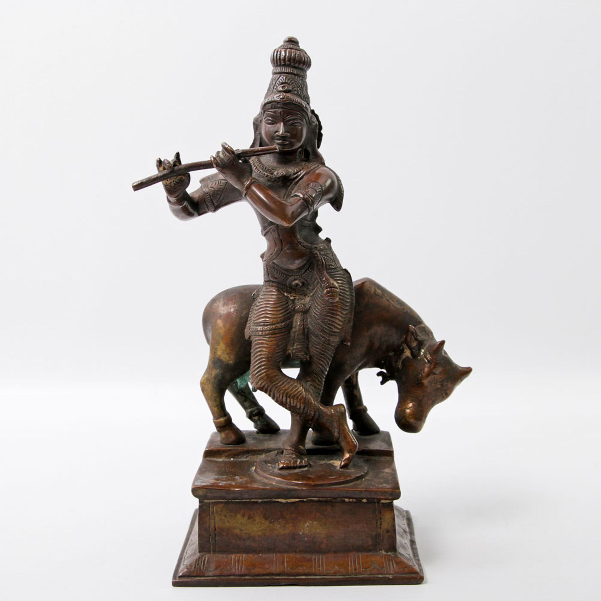 Bronze des Krishna als Kuhhirte. INDIEN, 1. Hälfte 20. Jh. auf rechteckigem Sockel vor einer Kuh