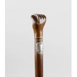 A late 19th century caved wooden walking cane, the handle formed as a clenched fist, the applied