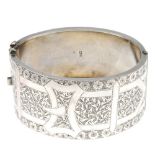 A late Victorian silver bangle. The wide hinged bangle engraved to one side with ivy and flowers