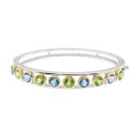 An 18ct gold gem-set hinged bangle. Of bi-colour design, the alternating peridot and aquamarine