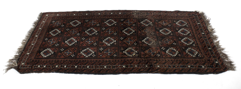 A Belouch-type Eastern rug. The brick red field with four rows of eight hooked lozenge-shaped
