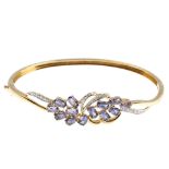 A 9ct gold sapphire and diamond bangle. Of foliate design, the oval-shape sapphire clusters, with