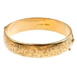 A mid 20th century 9ct gold hinged bangle. With scrolling motif front and plain half-bangle.