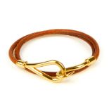 HERMÈS - a bracelet. Designed as a tan leather cord, with gold-tone metal hook terminal to one end