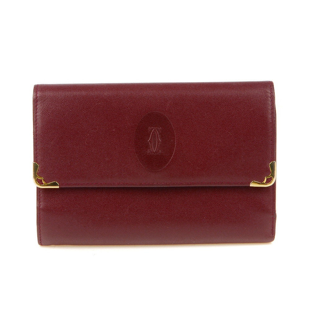 CARTIER - a Bordeaux leather purse. Designed with gold-tone corner guards and maker's embossed