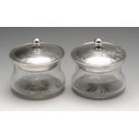 A pair of 1920's silver lidded powder pots, each of waisted clear glass form with star-cut base, the