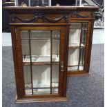 A small pair of Edwardian walnut glazed wall cabinets enclosed by a pair of bevelled glazed doors,