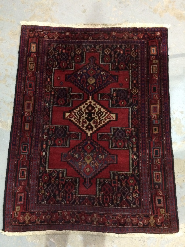 A Middle Eastern woollen rug, with three geometric motifs to the central red field,