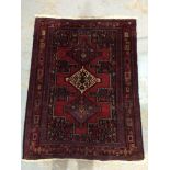 A Middle Eastern woollen rug, with three geometric motifs to the central red field,