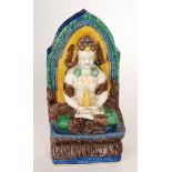 A polychrome model of a seated deity wearing gold coloured chains and holding a cone,
