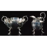 A George V hallmarked silver cream jug and sugar bowl of faceted form with leaf capped flying