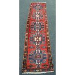 A 20th Century Middle Eastern runner, with five geometric motifs upon a red ground, 297cm x 74cm.