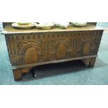A 17th Century style boarded oak coffer with lunette and arched carved panelled front on stiles,