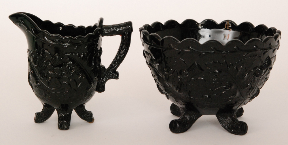 A late 19th Century Henry Greener black pressed glass sugar bowl the four swept feet below the wide