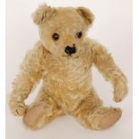 An early 20th Century golden mohair teddy bear with jointed limbs and with glass eyes, some wear,